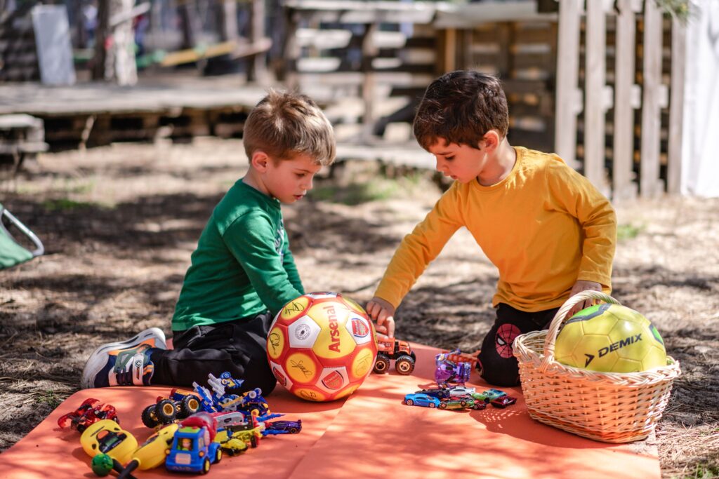 Young boys enjoy playtime with toy cars and soccer balls outdoors, capturing childhood joy.